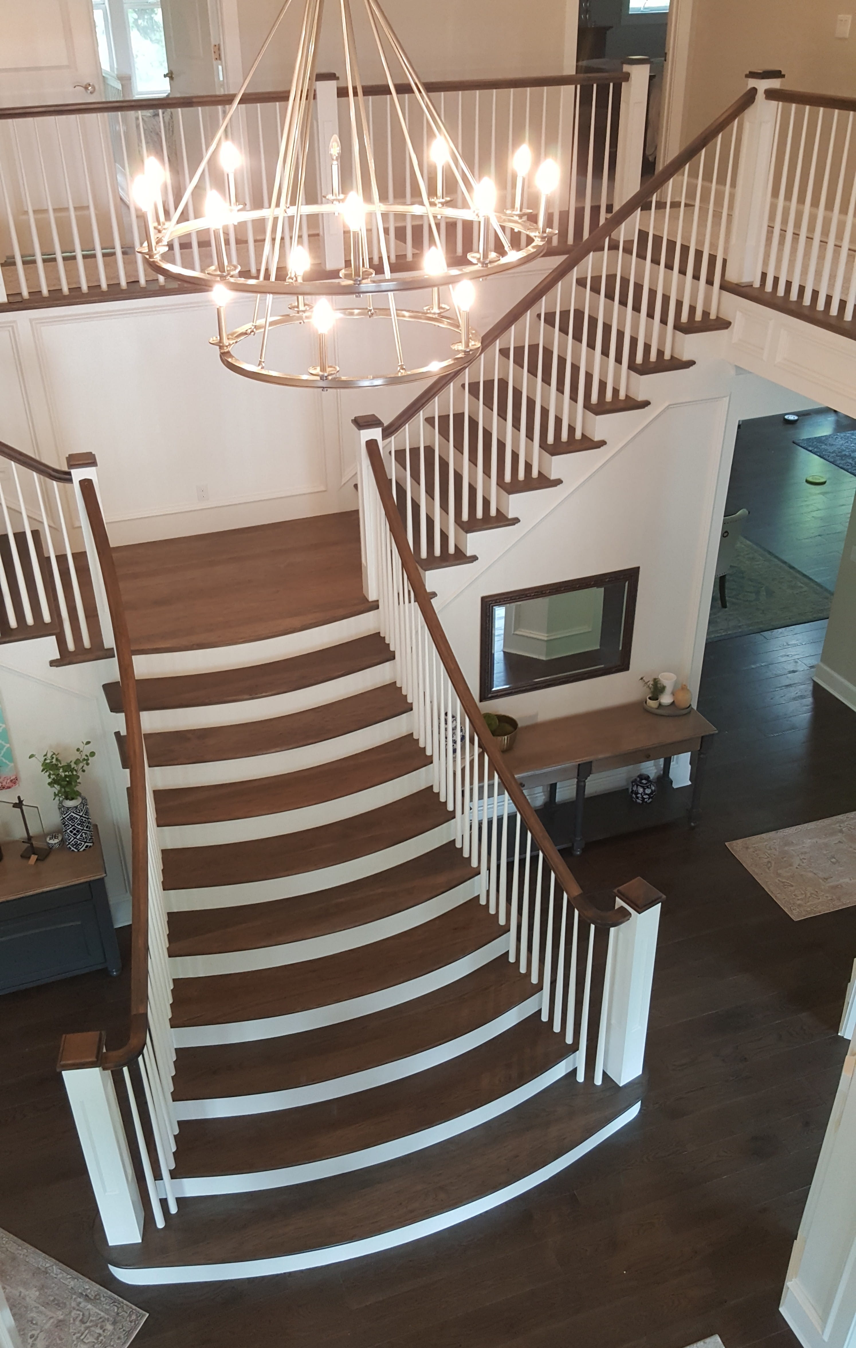 We removed the upper pony walls and staircase rails. Our team framed the mid and lower curved staircase to be code passing. All the wood parts, except the wood balusters, were manufactured, pre finished, sealed and installed by Staircrafters, Inc.